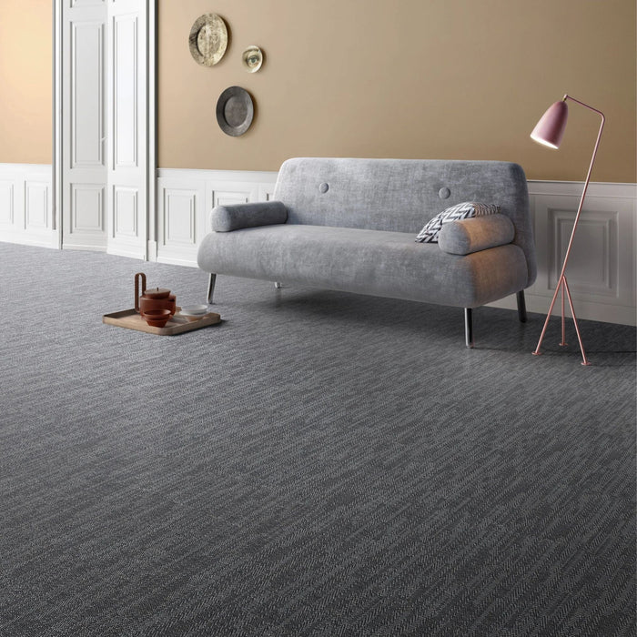 Textured charcoal fabric effect floor tiles with a light gray sofa, a pink floor lamp, and a small tray on the floor.